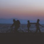 creative unfocused humans wallpaper pattern of fuzzy walking people silhouettes on dark twilight waterfront along Pacific ocean and unfocused mountain horizon background in evening sunset time