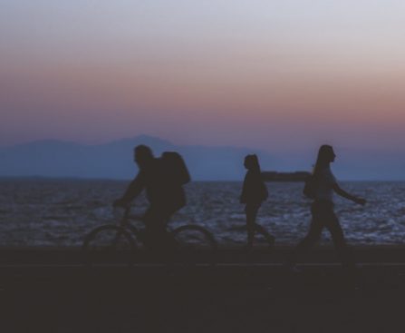 creative unfocused humans wallpaper pattern of fuzzy walking people silhouettes on dark twilight waterfront along Pacific ocean and unfocused mountain horizon background in evening sunset time