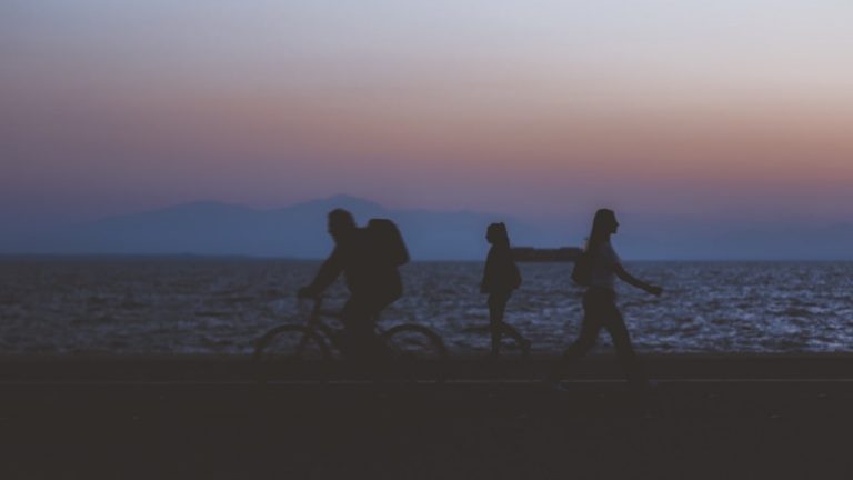 creative unfocused humans wallpaper pattern of fuzzy walking people silhouettes on dark twilight waterfront along Pacific ocean and unfocused mountain horizon background in evening sunset time