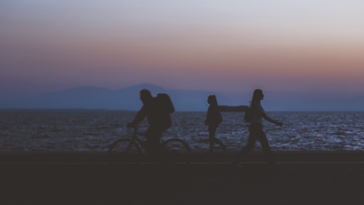 creative unfocused humans wallpaper pattern of fuzzy walking people silhouettes on dark twilight waterfront along Pacific ocean and unfocused mountain horizon background in evening sunset time