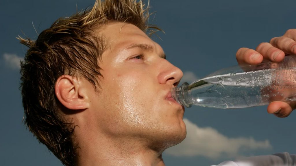 Close-up of a sweaty athletic man drinking water outdoors to cool off and stay hydrated.