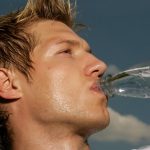 Close-up of a sweaty athletic man drinking water outdoors to cool off and stay hydrated.