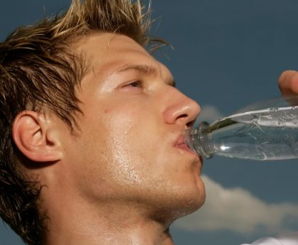Close-up of a sweaty athletic man drinking water outdoors to cool off and stay hydrated.