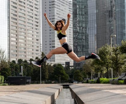 Woman leaping joyfully in an urban park, surrounded by towering skyscrapers.
